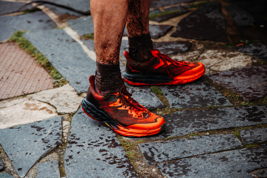 A photograph of a dirty pair of running shoes as an athletes stands at a checkpoint.